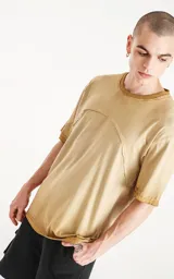 Remera oversize de algodón, color mostaza con efecto batik artesanal. Presenta costuras decorativas arqueadas que unen el cuello con los hombros y el torso.