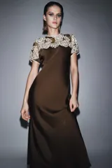 Vestido midi de viscosa color marrón oscuro, con cuello redondo y manga corta. Presenta un canesú de encaje floral color beige claro que cubre los hombros y parte superior del pecho. El bajo es evasé.