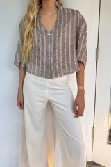 Blusa marrón con rayas verticales blancas y bordado de hojas. Tiene cuello mao con volados, mangas 3/4 y cierre frontal con botones.