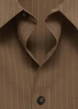 Camisa marrón con rayas verticales finas, de corte oversize, manga larga con puños abotonados, cuello camisero, bolsillo de parche en el pecho y cierre frontal con botones.