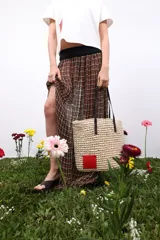 Bolso de rafia color beige con asas de cuero marrón y parche rojo en una esquina.