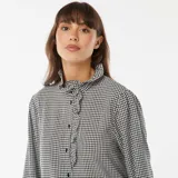 Camisa de manga larga con estampado vichy en blanco y negro, cuello alto con volantes y cierre frontal con botones.