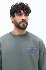 Buzo de algodón color beige claro, con cuello redondo y puños. Presenta un estampado grande en la espalda con texto en gris y blanco, incluyendo referencias a 'London', 'Southbank Art Gallery Centre' y una representación estilizada de la bandera del Reino Unido.