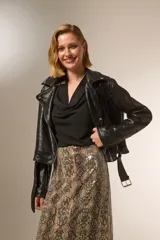 Chaqueta negra de eco-cuero con cuello solapa, cierre frontal asimétrico y cinturón ajustable. Incluye bolsillos laterales con cierre y detalles de tachas plateadas en cuello y solapa.