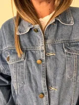 Campera de jean celeste con corte corto y fit relajado, botones metálicos frontales, bolsillos con solapa y espalda con elástico fruncido.