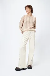 Pantalón de denim blanco con calce wide leg y ruedo desflecado. Presenta tachas metálicas a lo largo de los laterales.