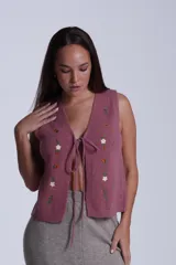 Chaleco tejido color crema con escote en V y cierre frontal con lazos. Presenta bordados de flores en tonos naranja, verde y blanco.