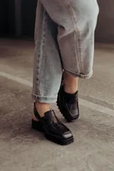 Zueco negro con textura croco, diseño tipo mocasín y tira regulable al talón.