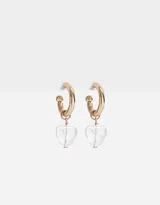 Aros dorados tipo argolla con dije colgante de cristal transparente en forma de corazón.