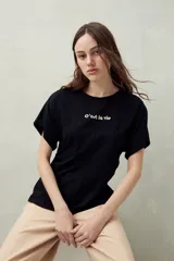 Remera blanca de manga corta con bordado frontal "C’est la vie", calce relajado y frunces laterales.