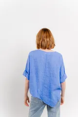 Blusa color naranja confeccionada en 100% lino, con escote en V, mangas cortas con vuelta y silueta amplia. Presenta terminación asimétrica y fila de botones decorativos en uno de los hombros.