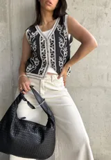 Chaleco negro con bordado floral blanco, escote en V, cierre frontal con botones y ribete de encaje.