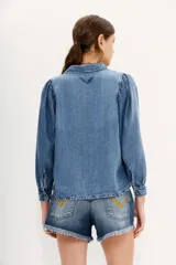 Camisa celeste de tencel con calce recto, manga larga amplia con frunces en los hombros y cuello camisero. Mangas terminadas en puño con botón y ojal. Cartera delantera con botones metálicos con el logo de la marca.