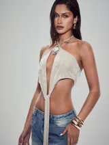 Top halter color beige claro, con escote profundo en V que se anuda en la parte inferior. Presenta un dije metálico con forma de espiral y centro nacarado en el centro del escote.