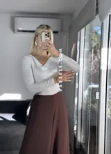 Blusa blanca de poliéster labrado, con cuello drapeado estilo bote y mangas largas.