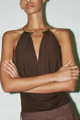 Body marrón de tejido de punto con escote drapeado y collar metálico con apliques de strass. Tiene forro interior y cierre inferior con botones a presión y cierre lateral con cremallera oculta.