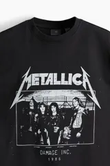 Remera negra de algodón con estampado del logo de Metallica y la imagen de la banda Damage Inc. 1986. Corte oversized con cuello redondo ribeteado, hombros caídos y bajo recto.