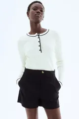 Short negro de tiro alto con cierre y pretina prolongada con botón. Modelo con bolsillos al bies y bolsillos insertados decorativos atrás.