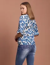 Blusa blanca de gasa marca Sioni, con cuello a la base y escote en V. Tiene abertura central con botones y mangas 3/4 con terminación fruncida.
