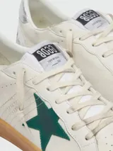 Zapatillas Golden Goose modelo Ball Star, color blanco con detalles en verde y plateado. Confeccionadas en cuero con efecto desgastado, presentan una estrella verde en el lateral, talón plateado y suela de goma color caramelo.