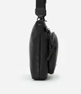 Bolso tipo postman negro, confeccionado en poliuretano, con bolsillo delantero y correa ajustable.