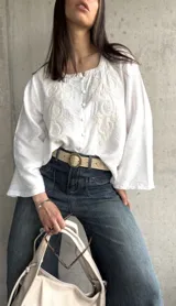 Blusa blanca de manga larga acampanada con bordado floral en el frente y cierre con botones.