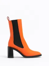 Botín Chelsea de caña media color naranja, con elásticos laterales negros y tacón bloque negro.