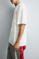 Camiseta blanca de corte holgado con cuello en V y mangas cortas. Presenta un diseño de malla con diferentes texturas combinadas a tono y estampado frontal con la inscripción "Legacy Crew 95 Elite Mode".