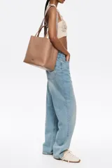 Bolso tote negro de cuero vacuno con doble asa corta y correa de tela extraíble. Interior con tres compartimentos y bolsillo con cremallera. Logo metálico de la marca en el frente.