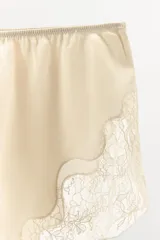Shorts tipo lencero color crema confeccionado en tejido satinado con tiro alto, cintura elástica y detalle de encaje a tono en el ruedo.