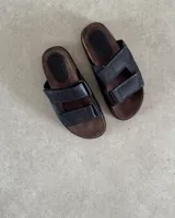 Sandalias bajas de cuero negro con dos tiras anchas sobre el empeine y plantilla marrón.