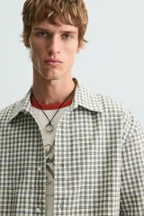 Camisa de hombre de corte boxy fit, confeccionada en tejido de algodón a cuadros en tonos beige, verde y azul. Tiene cuello solapa, manga corta y cierre frontal con botones.