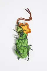 Colgante para bolso tejido a crochet, con forma de flor amarilla y naranja sobre un cuerpo verde con detalles en verde oscuro. Tiene un cordón marrón para colgar.