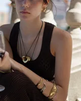 Collar con dije dorado irregular con agujero central, colgando de cordón negro ajustable.