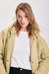 Campera capitoneada color verde claro, con capucha y cierre frontal con botones a presión. Tiene bolsillos laterales y cordón ajustable en el ruedo.