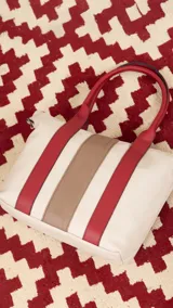 Cartera de mano color beige con divisiones y detalles en marrón y blanco. Tiene correa corta, correa larga ajustable, bolsillo trasero y bolsillos internos.