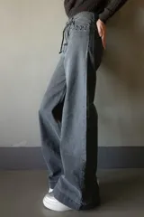Pantalón de jean azul oscuro de pierna ancha con detalle de trenzado en bolsillos y cinturón.