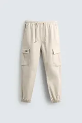 Pantalón cargo color beige de corte slim fit, con cintura elástica ajustable con cordón, bolsillos frontales, bolsillos traseros de vivo y bolsillos laterales tipo plastrón con solapa.