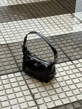 Cartera negra charolada con asa corta y cierre de cremallera. Tiene un aplique metálico en forma de estrella.