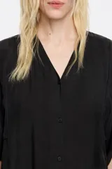 Vestido midi negro de corte recto, con escote en V pronunciado en delantero y espalda, manga corta recta con bajo descosido, cierre frontal con botonadura y fruncidos laterales en el bajo.