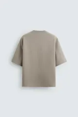 Camiseta color visón de corte relaxed fit, confeccionada en tejido interlock de algodón con elasticidad. Tiene cuello redondo, manga corta y estampado frontal con textura combinada a contraste en color negro.