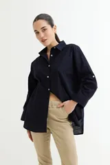 Camisa blanca de corte amplio, con cuello clásico, cierre frontal con botones y mangas largas con puños abotonados.