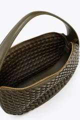 Bolso de mano color verde militar con efecto trenzado y asa corta. Incluye correa extraíble para usar como bandolera y cierre de cremallera metálica.