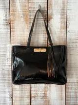 Cartera tipo tote de cuero gamuzado en color marrón, con textura de efecto cocodrilo. Presenta un cierre frontal metálico en tono dorado y un detalle de flecos colgantes en el lateral. Cuenta con doble asa de hombro.