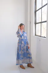 Vestido largo celeste con estampado floral en tonos beige, corte amplio, cuello camisero y mangas largas.