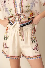 Short de seda color crema con estampado floral y detalles geométricos en los bordes. Tiene cintura elástica con cordón ajustable.