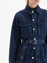 Parka larga de denim azul oscuro, con cuello camisero, bolsillos delanteros con tapa y cinturón ajustable con arandelas metálicas.