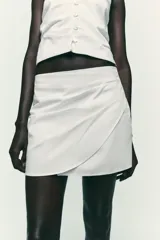 Falda pantalón negra de tiro alto con delantero cruzado y pliegues. Cierre trasero con cremallera oculta.