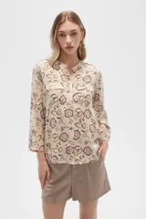 Camisa de viscosa color crema con estampado floral en tonos rosa, verde y marrón. Tiene cuello mao, mangas largas con puños abotonados, cierre frontal con botones y dos bolsillos con solapa en el pecho.