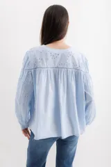 Camisa celeste de algodón con bordado calado, cuello en V y mangas largas abullonadas con puños elásticos.